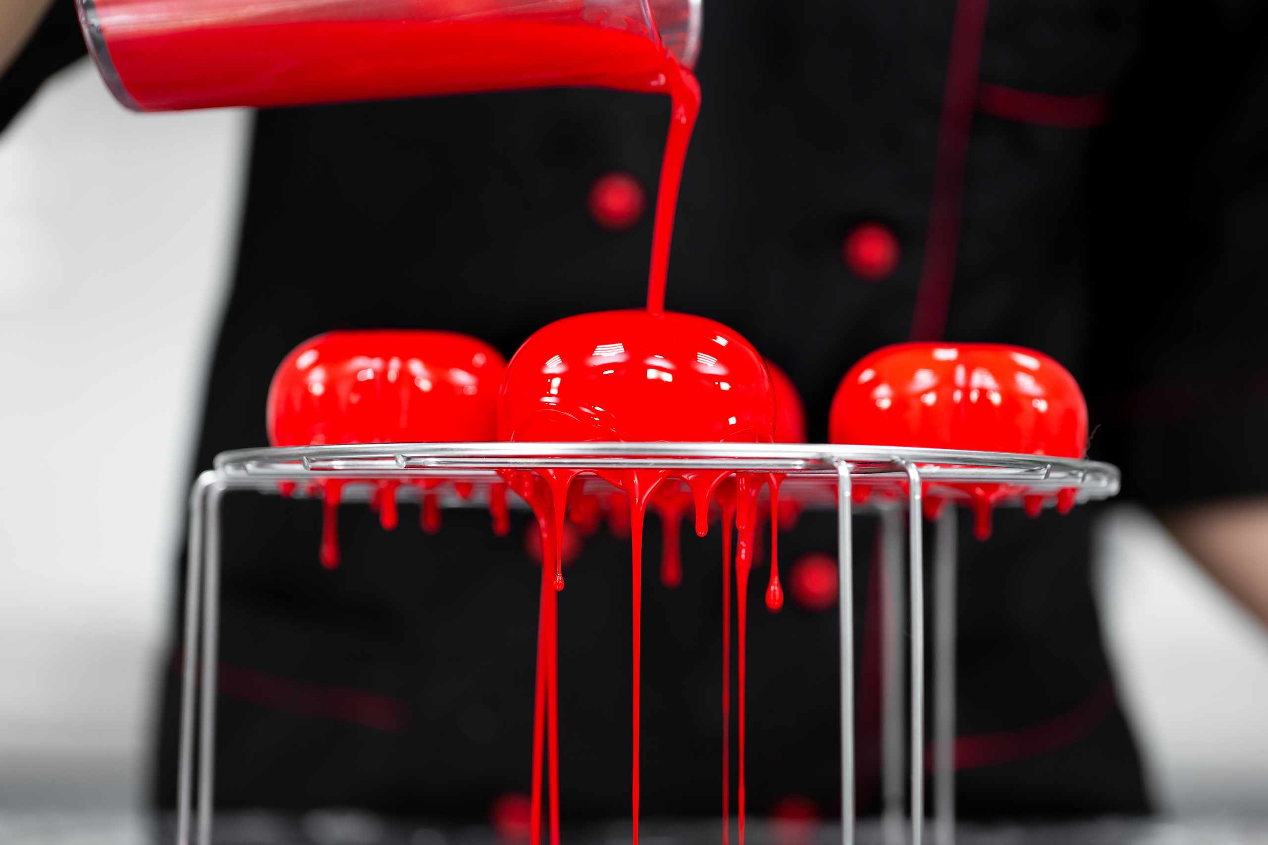 Chef pouring red glaze over desserts